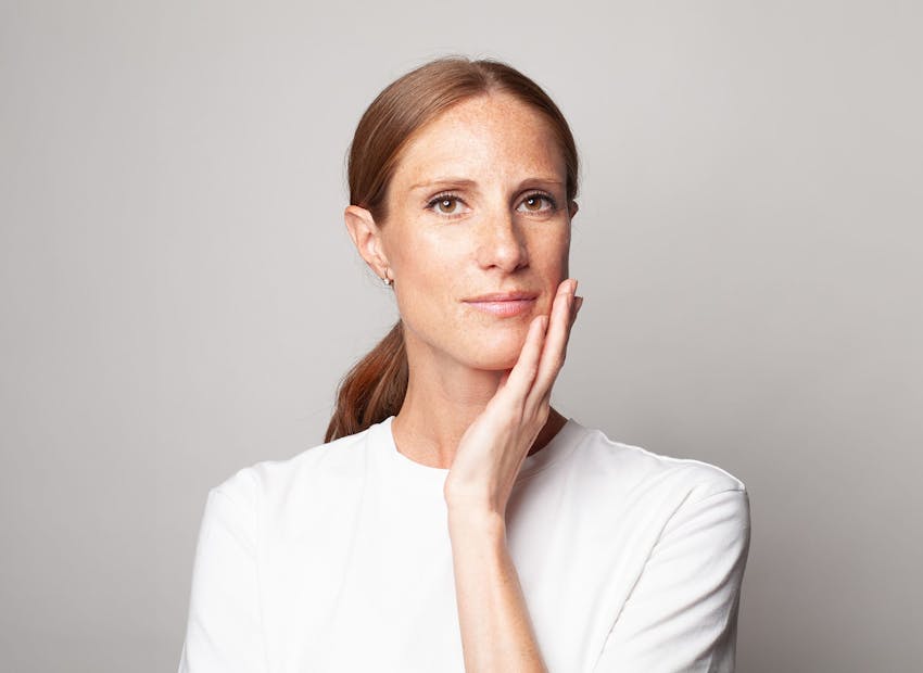 woman in white shirt touching her jaw with low ponytail