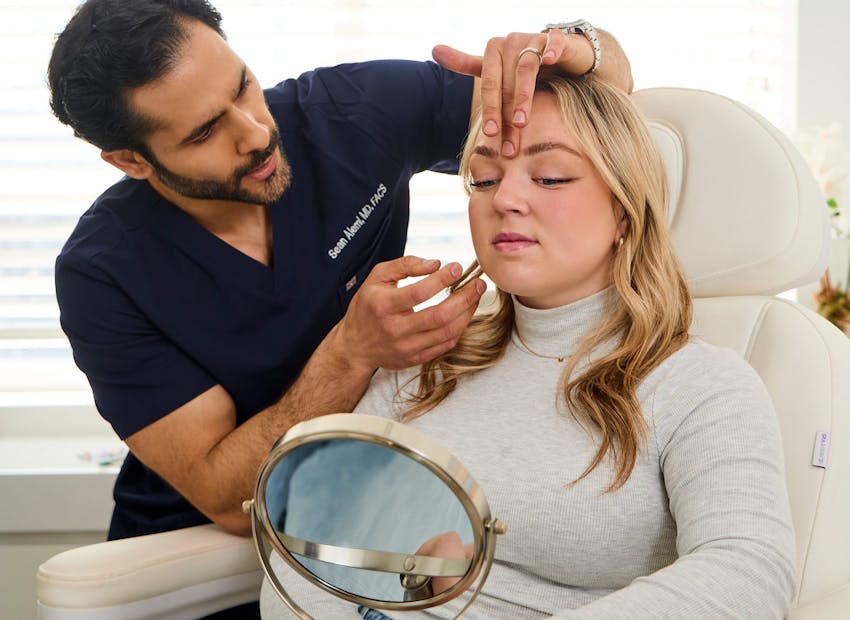 Dr. Alemi with his finger on client's forehead while she looks at handheld mirror