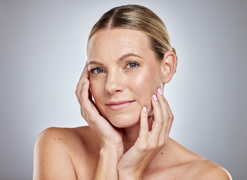 woman with hair tied back and hands on her face