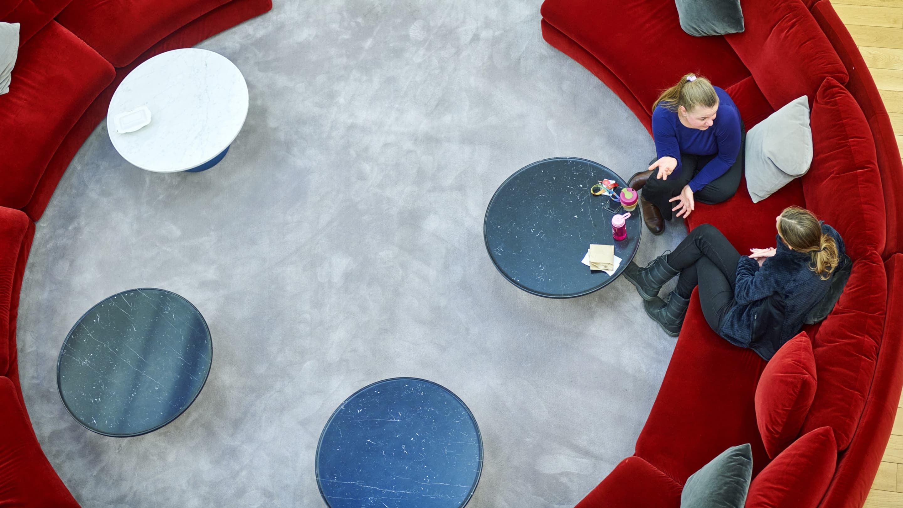 Top-down view of two colleagues in discussion on red circular seating with small round tables.