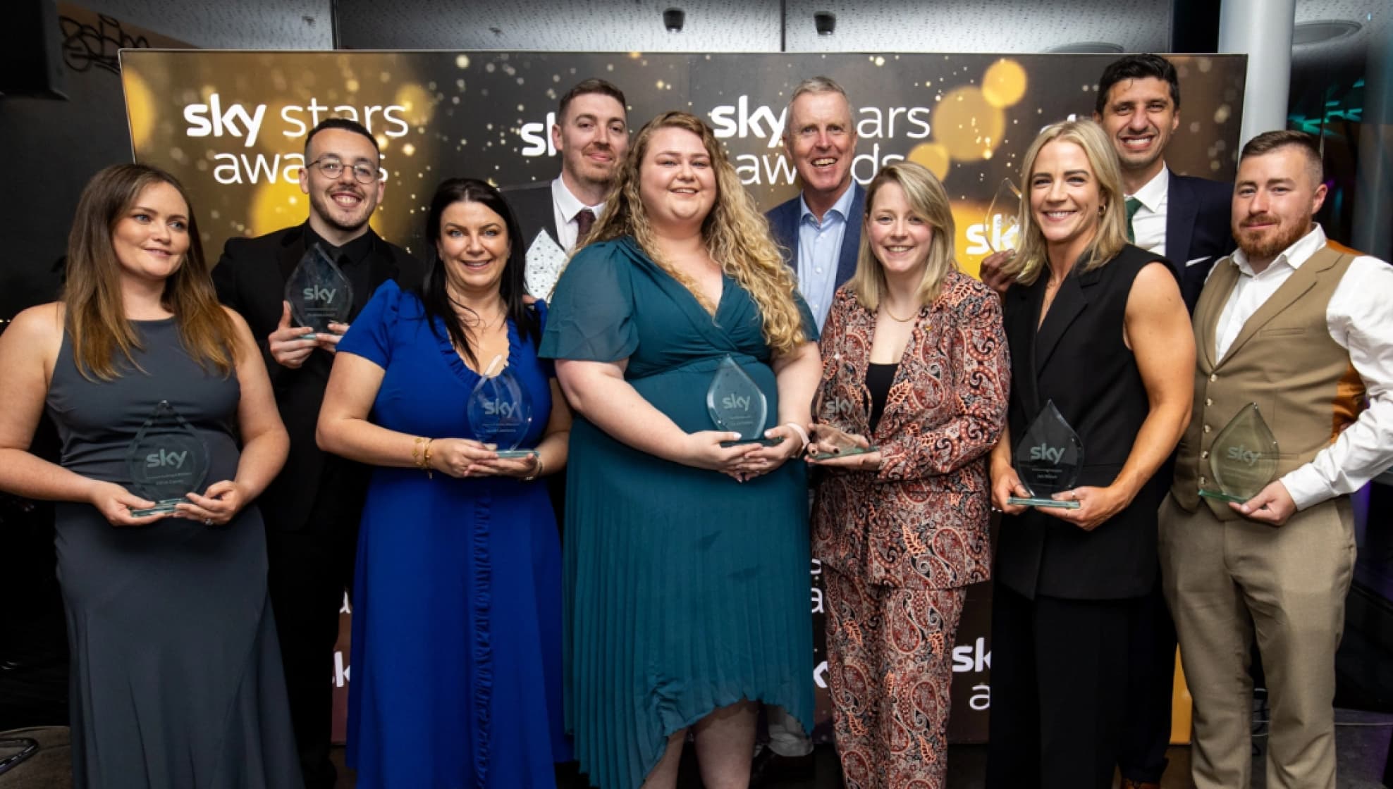 Group of award winners stand proudly holding trophies in front of a Sky Stars Awards banner.