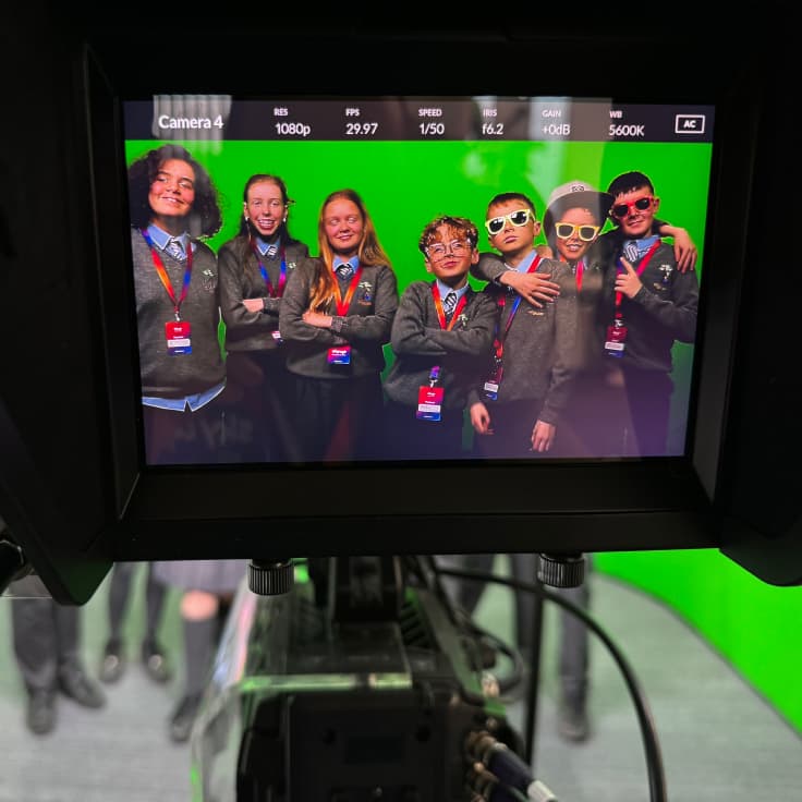A camera positioned in front of a vibrant green screen, with kids in sunglasses posing in front, ready for video production