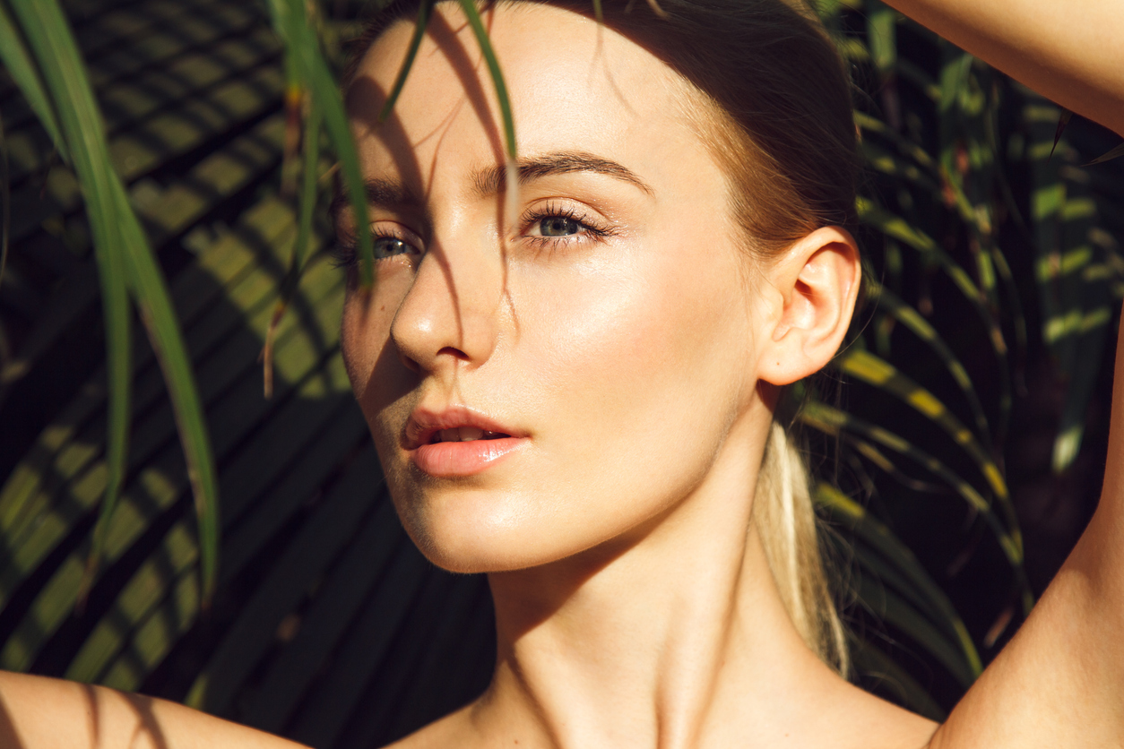 young woman with perfect skin hiding under palm leaf