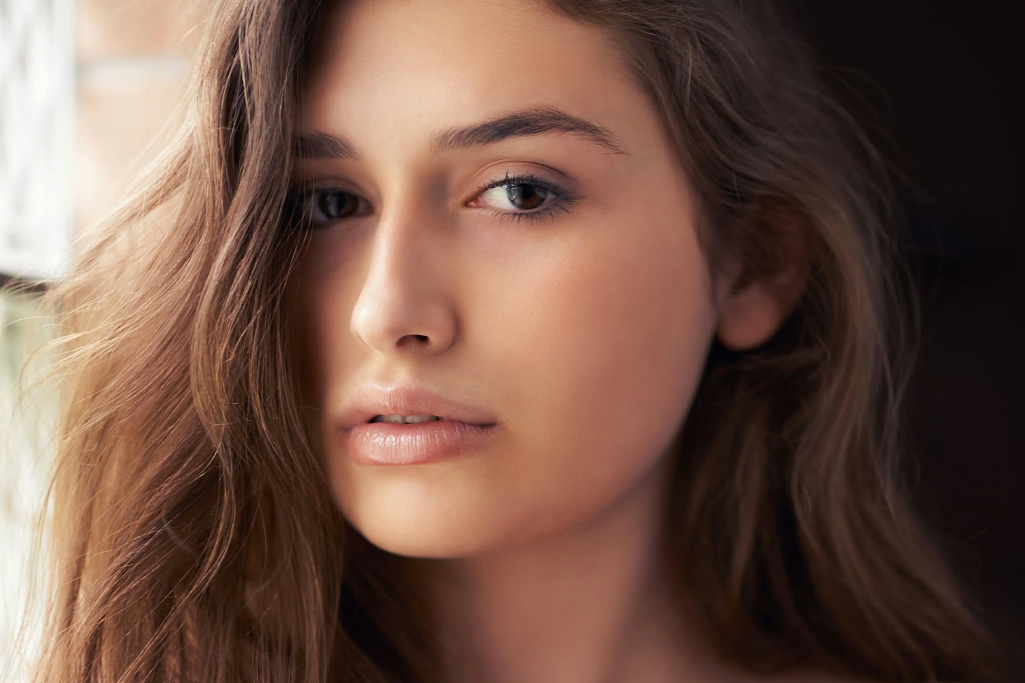 woman with brown hair looking forward with hand near collarbone