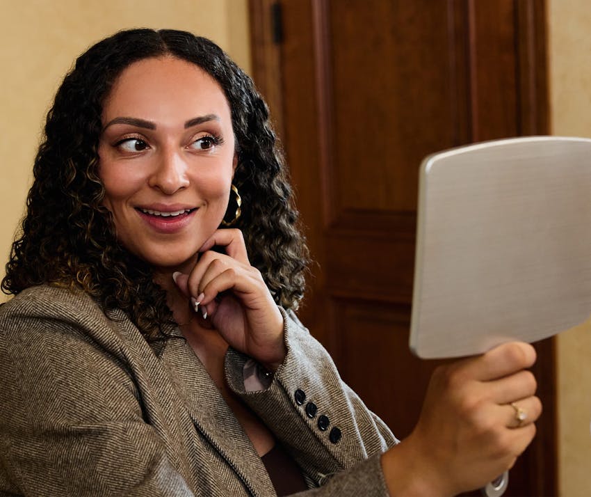 Woman smiling into hand mirror