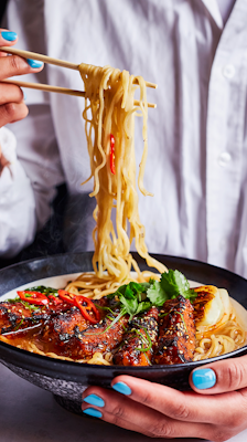woman using chopsticks to each ramen noodles