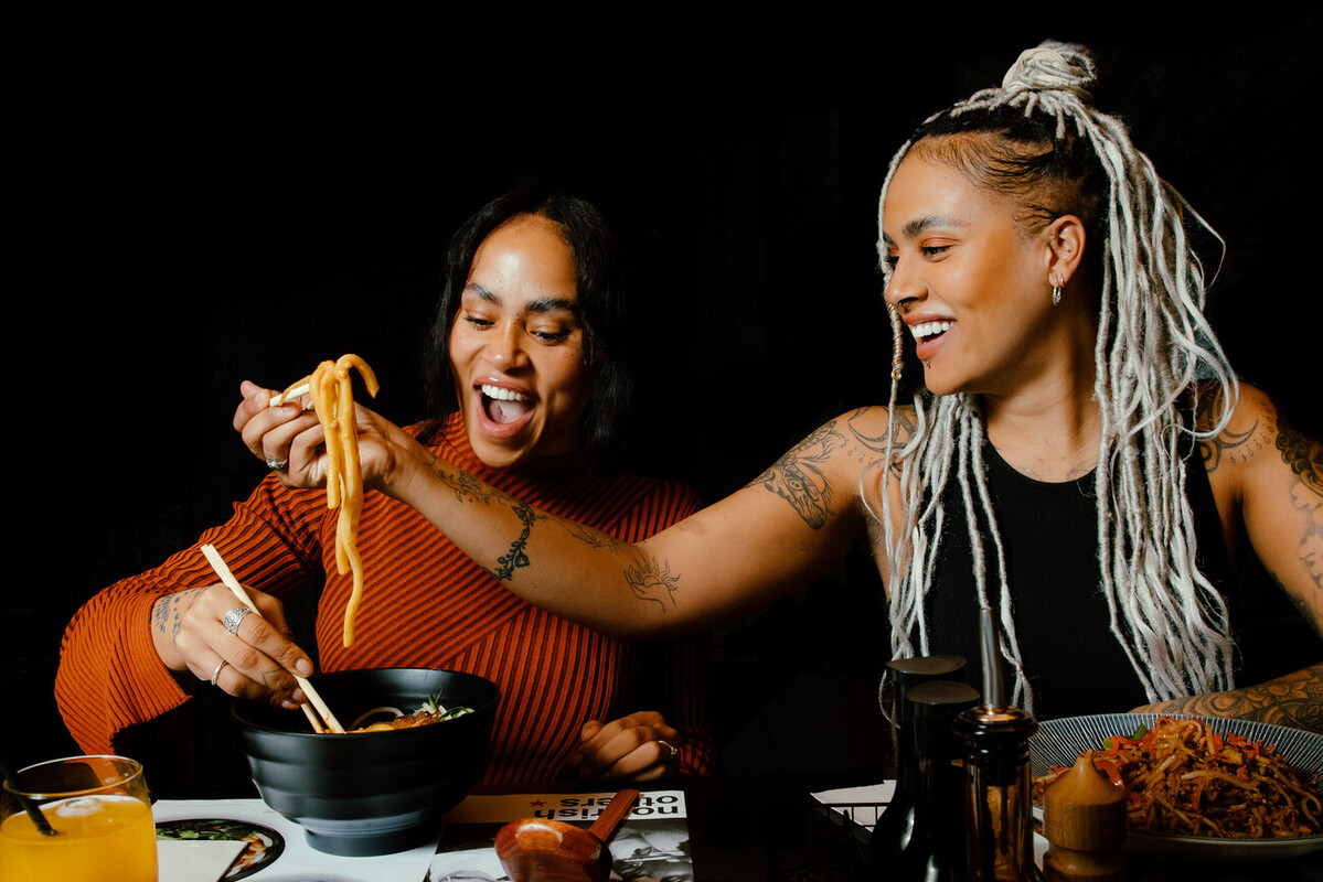 two women eating udon noodles with chopsticks