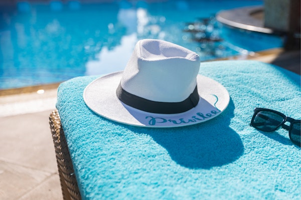 A Guide to Privilee Guest Passes A white hat and sunglasses on a towel beside a pool.