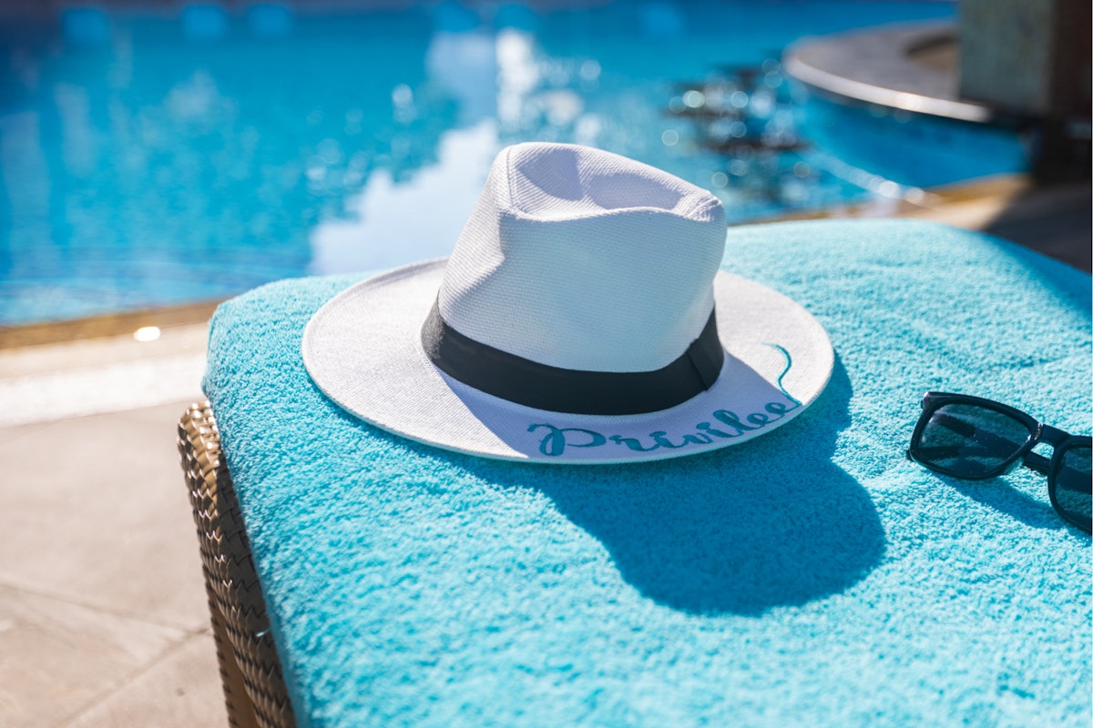 A white hat and sunglasses on a towel beside a pool.