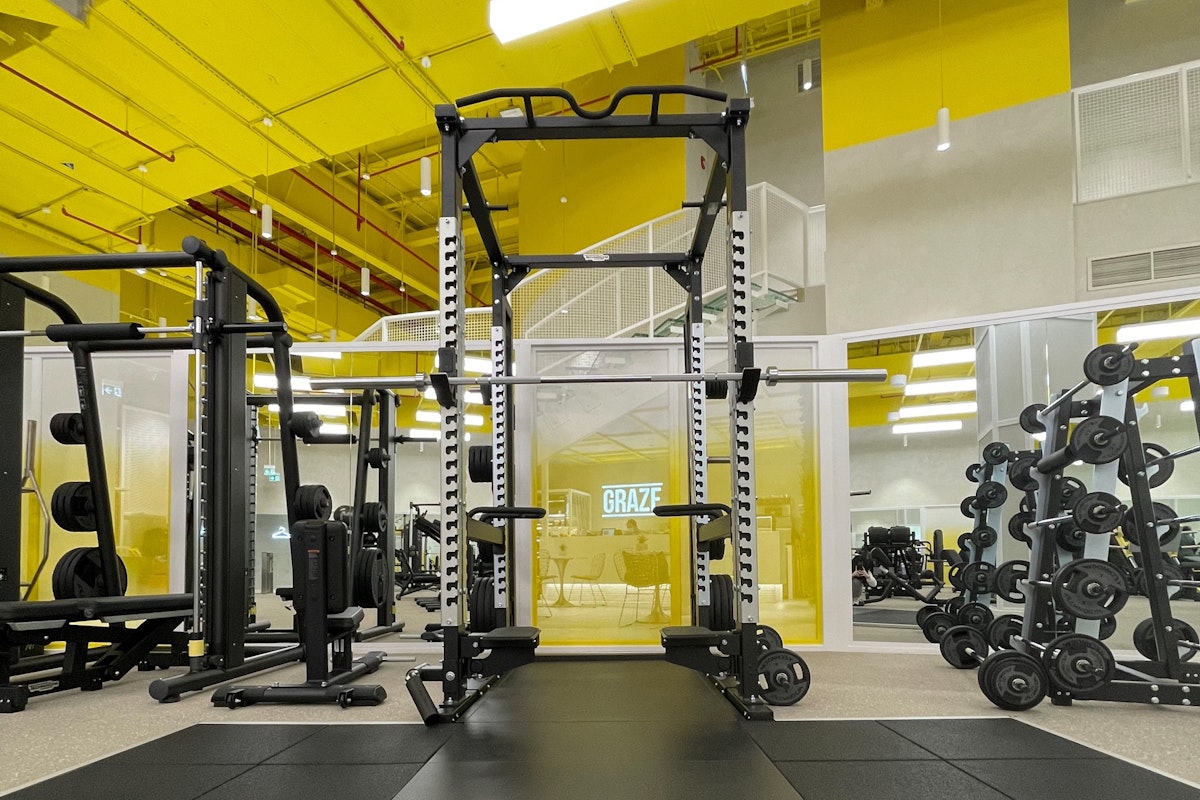 Modern gym with workout machines, free weights, and bright yellow ceiling accents