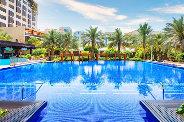 Outdoor swimming pool surrounded by palm trees and a tropical resort.
