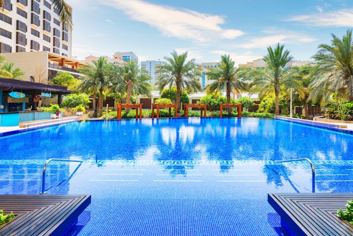 Outdoor swimming pool surrounded by palm trees and a tropical resort.