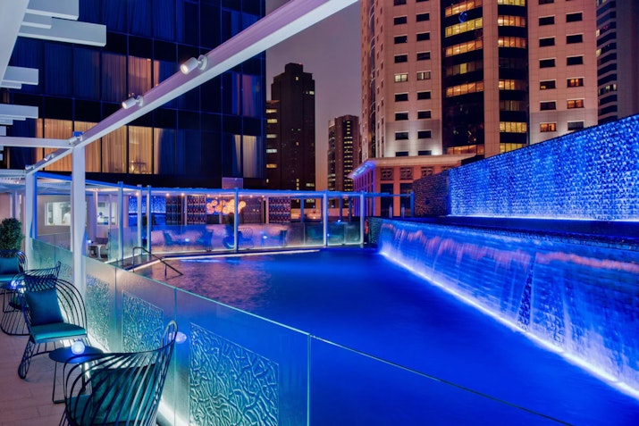 Rooftop pool with blue lighting and city skyline at night