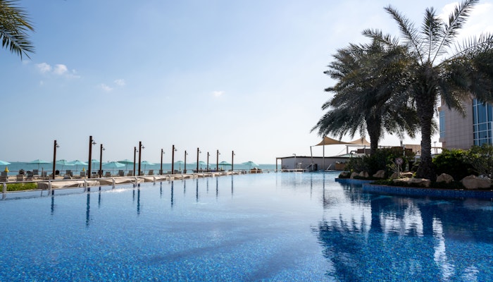 Hilton Doha West Bay Infinity pool with palm trees, overlooking the ocean and clear blue sky.