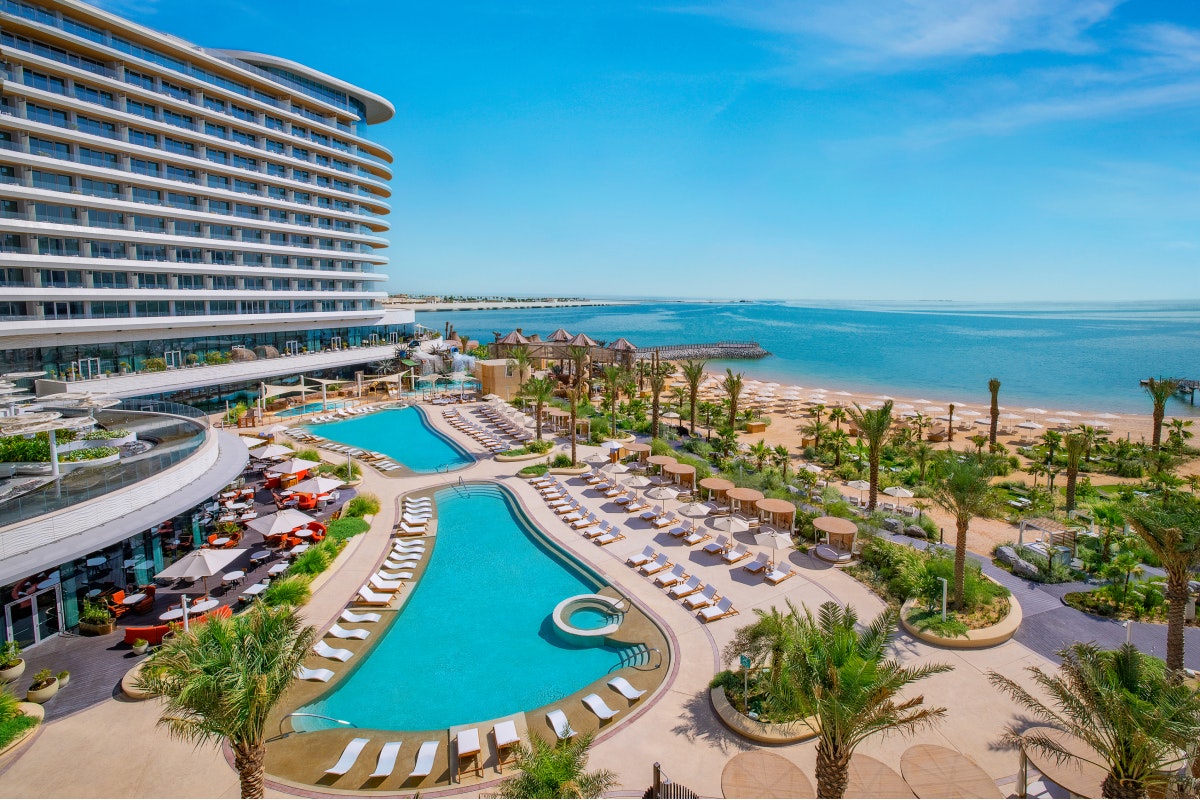 Waldorf Astoria Lusail Resort with two swimming pools, palm trees, lounge chairs, and a beach view