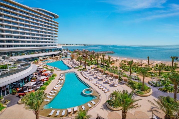 Resort with two swimming pools, palm trees, lounge chairs, and a beach view