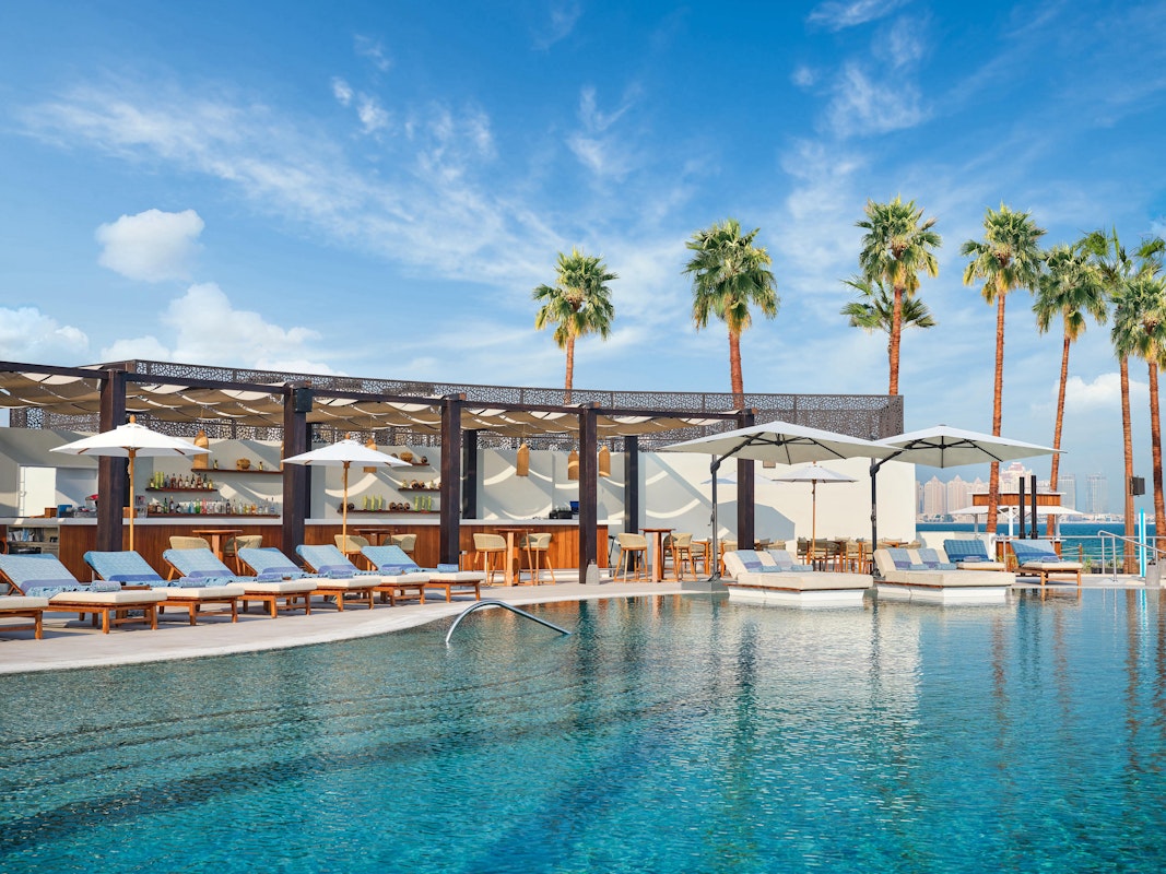 Resort pool surrounded by lounge chairs, palm trees, and shaded cabanas under a blue sky