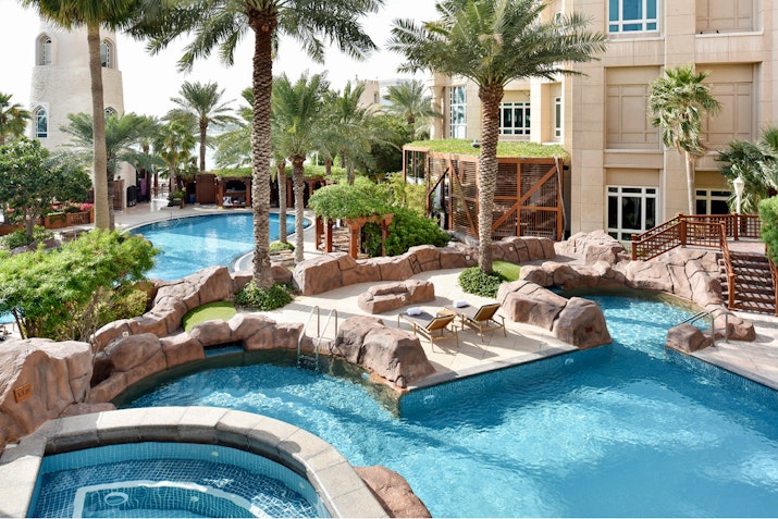 Resort pool with rock features, palm trees, and tropical landscaping.