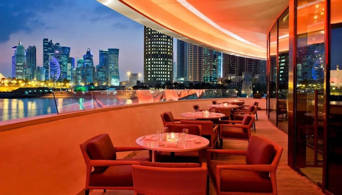 Nobu Doha at Four Seasons Hotel Outdoor restaurant seating with a stunning view of the city skyline and illuminated buildings at night