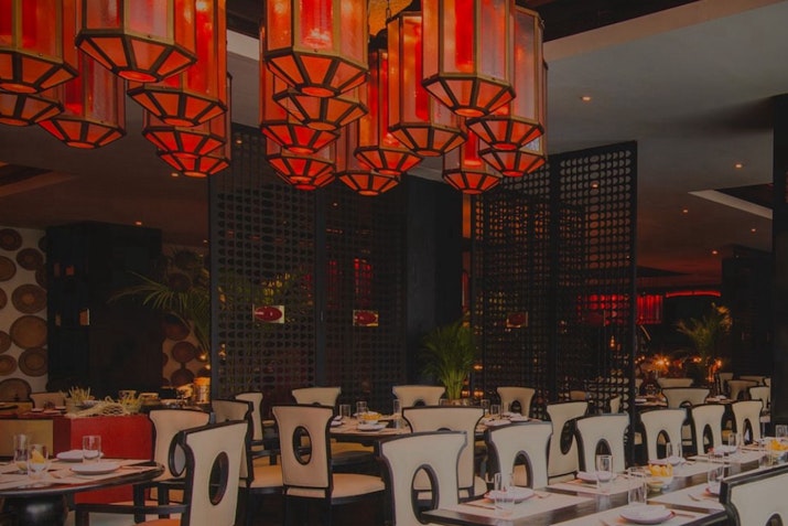 Modern restaurant with red lighting and elegant dining tables set for guests
