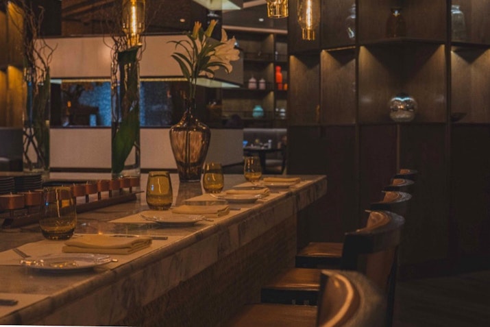 Intimate dining setup with a marble bar counter, glassware, and decorative lighting.