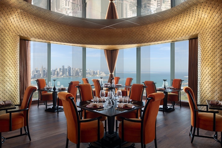 Elegant restaurant interior with tables set for dining, offering a panoramic view of the city and sea.