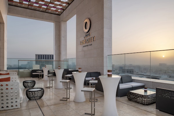 Rooftop lounge with seating, tables, and a sunset view over the city skyline.