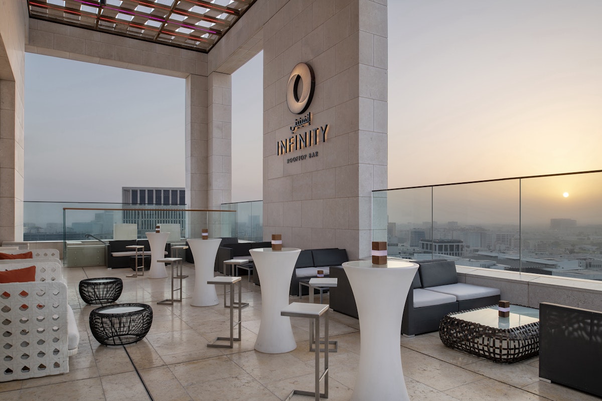 Rooftop lounge with seating, tables, and a sunset view over the city skyline.