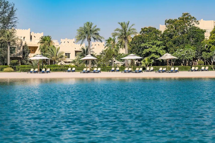Serene beach scene with umbrellas and lounge chairs along the shore, surrounded by lush greenery and clear blue water.