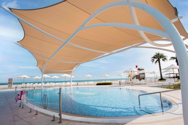 Outdoor pool with a shaded canopy and beach umbrellas, overlooking the ocean.