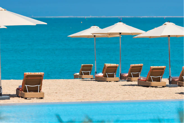Privilee’s Guide to beating the heat in Qatar Beachfront view with lounge chairs under umbrellas, overlooking the turquoise sea.