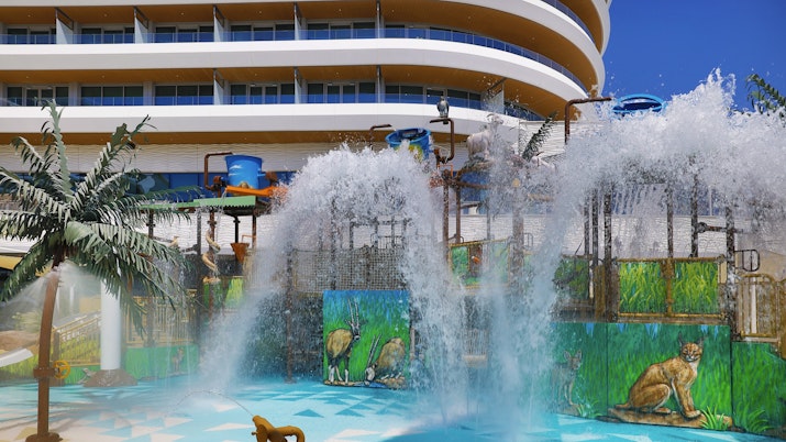 Water play area with large water features, colorful animal-themed murals, and a hotel building in the background.