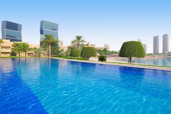 Outdoor pool with clear blue water, palm trees, and modern buildings in the background