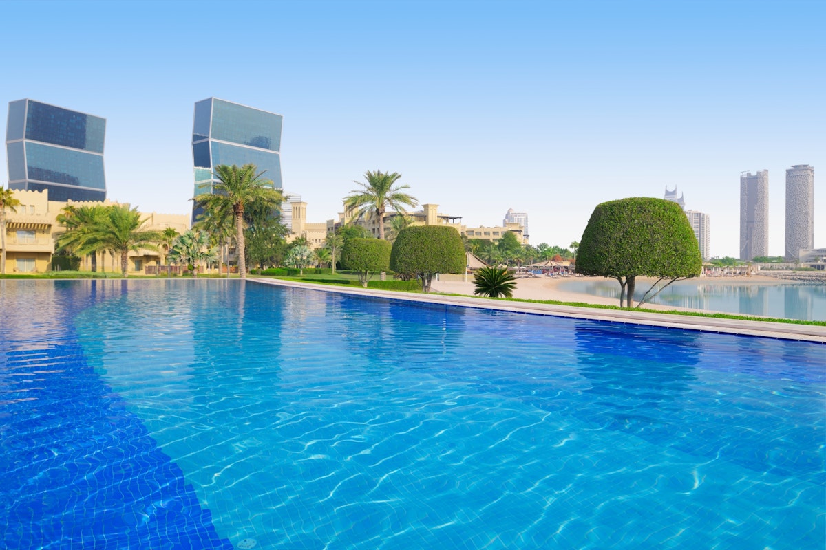 Outdoor pool with clear blue water, palm trees, and modern buildings in the background