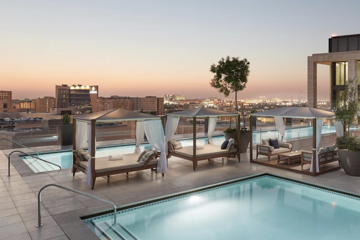 Rooftop pool with lounge cabanas and city skyline views at sunset