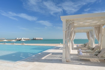 Beachfront pool with white cabanas, clear turquoise water, and a sunny sky.