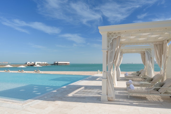 Beachfront pool with white cabanas, clear turquoise water, and a sunny sky.