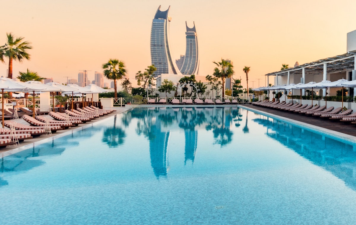 Luxury pool with lounge chairs, palm trees, and a city skyline with iconic skyscrapers at sunset.