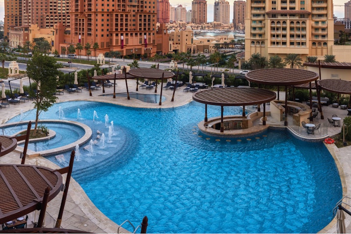 Resort-style pool with cabanas, water fountains, and a view of surrounding buildings.