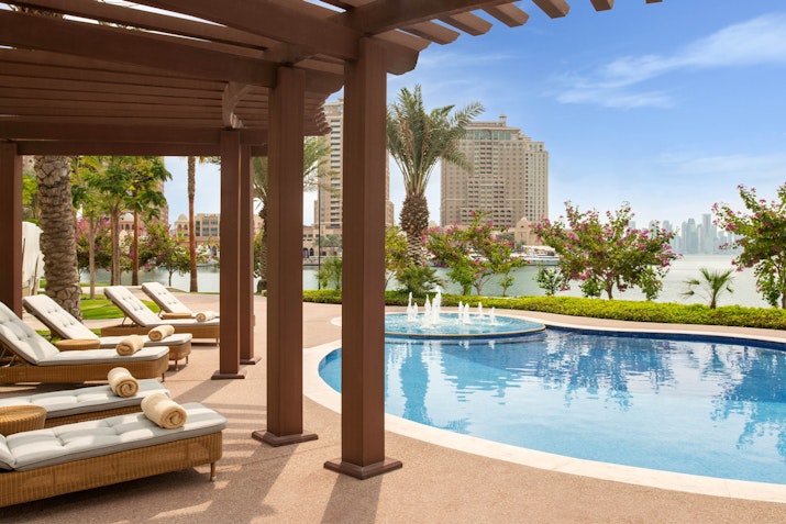 Poolside lounge area with chairs and a view of palm trees and the skyline.
