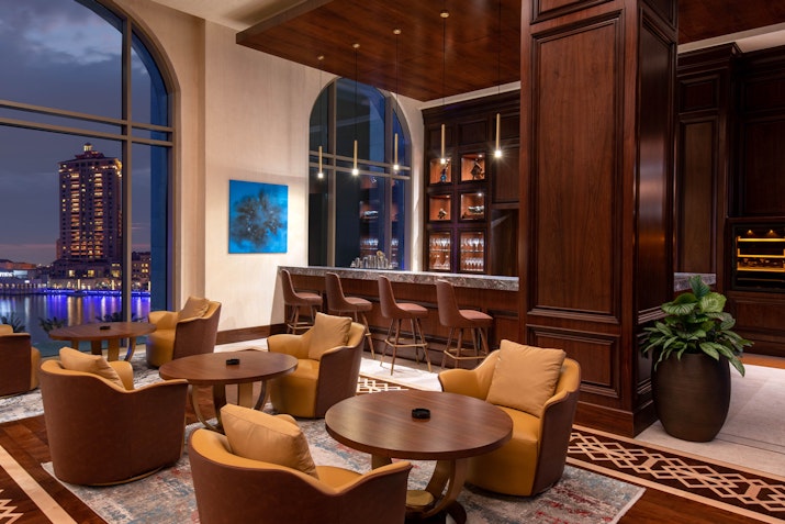 Luxurious bar and lounge area with wooden decor, plush seating, and city view at dusk