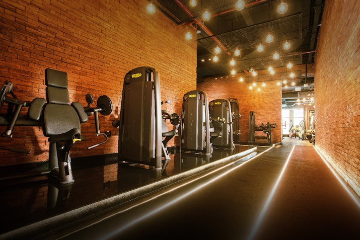 Industrial-style gym with brick walls, exercise machines, and ambient lighting.