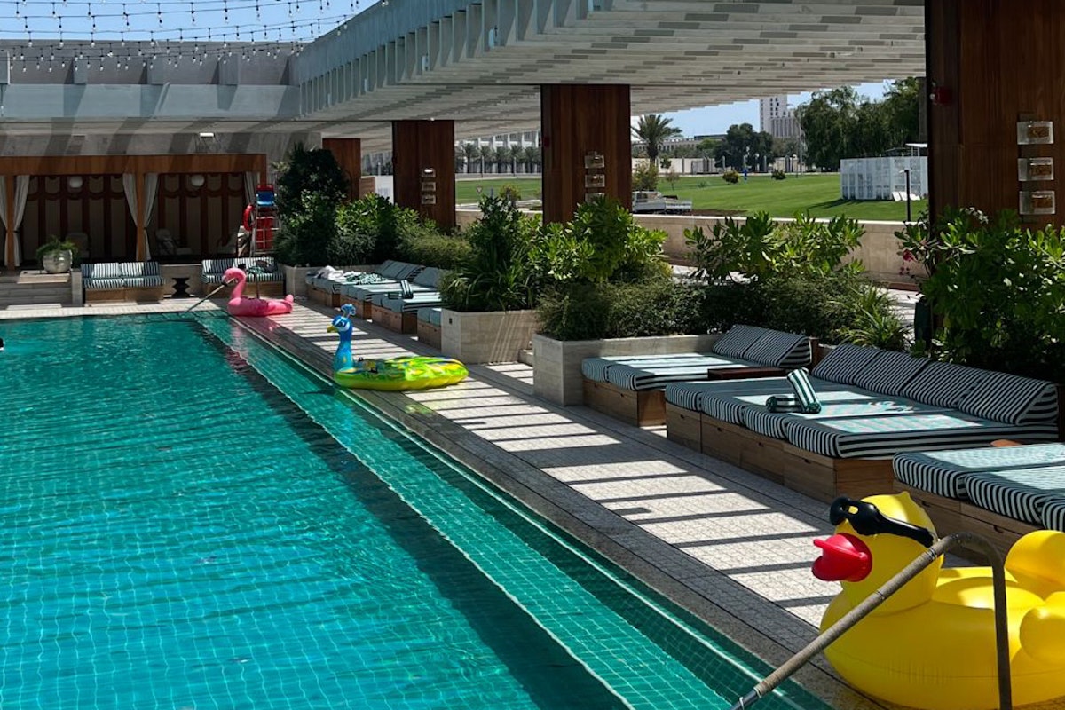 Swimming pool with inflatable ducks and loungers, surrounded by greenery and sunlight