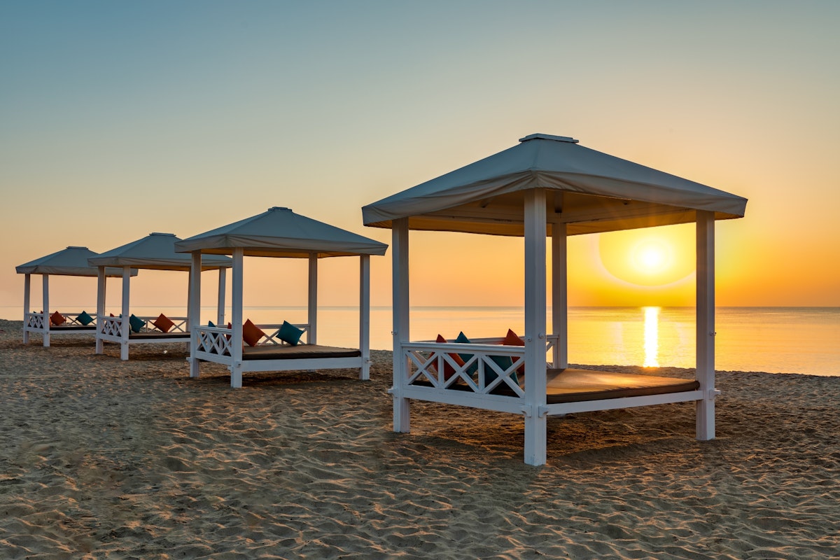 Beachside gazebos with cushions, set against a beautiful sunset over the ocean