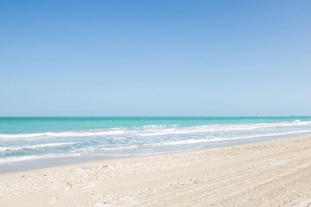 Enjoy complimentary Nanny access to these Privilee Venues Clear turquoise ocean waves lapping onto a sandy beach under a bright blue sky.
