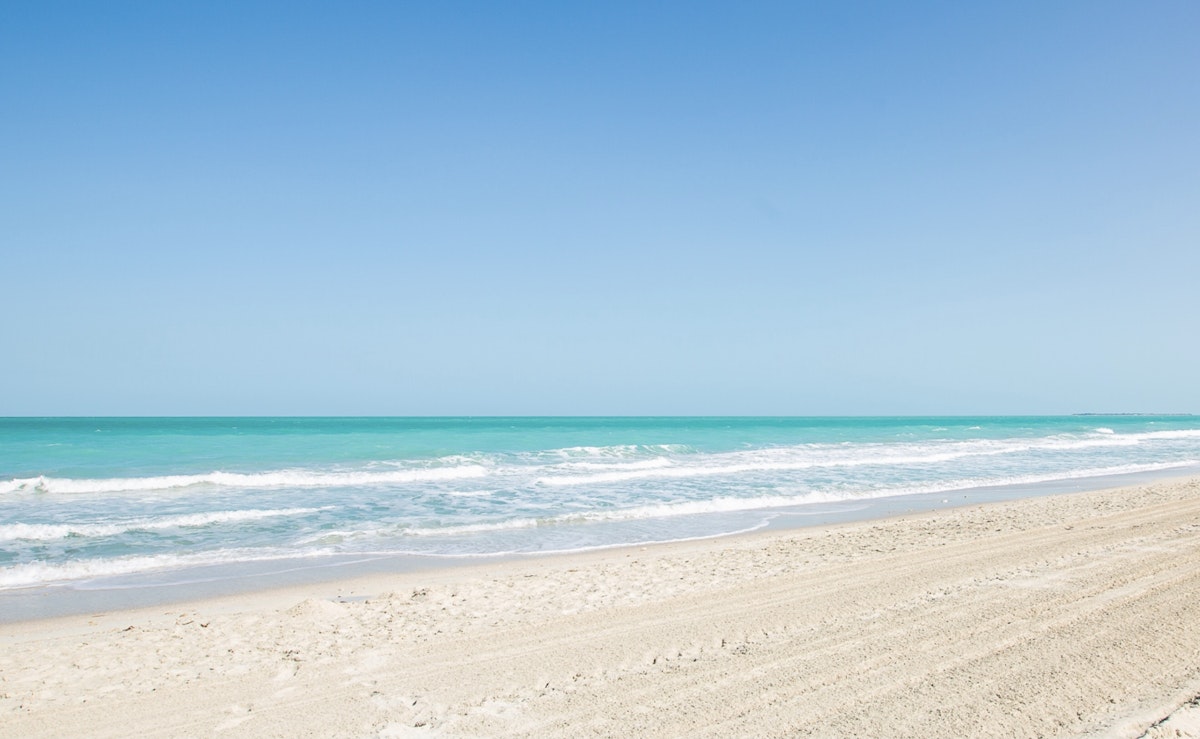 Clear turquoise ocean waves lapping onto a sandy beach under a bright blue sky.