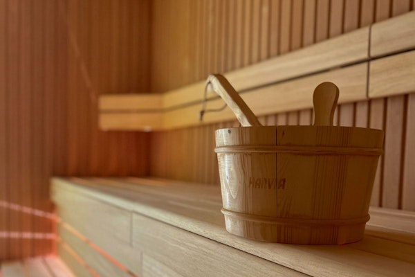 Wooden sauna bucket with ladle on a wooden bench, bathed in warm light.
