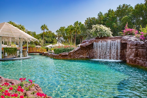 Pool with waterfall and pavilion surrounded by greenery and flowers.