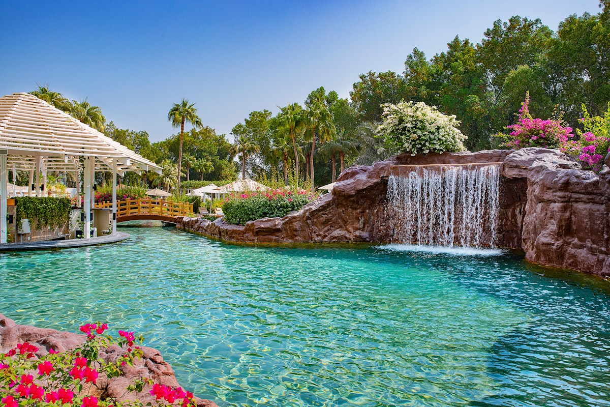 Pool with waterfall and pavilion surrounded by greenery and flowers.