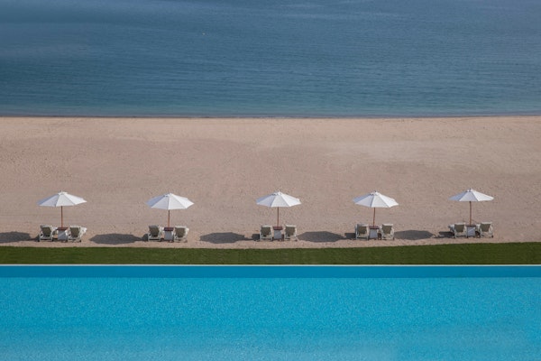 The Chedi Katara Hotel & Resort View of beach lounge chairs with umbrellas next to a swimming pool and ocean.